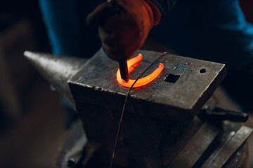 Blacksmith forges and making metal horseshoe with hammer and anvil at forge.