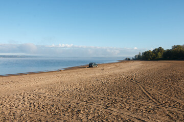 A deserted beach with a car at the water's edge.