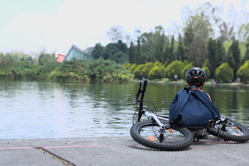 Boy squatting in front of a lake with his bike and backpack behind