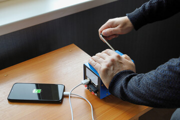 Human hands rotate handle of electricity generator, charge smartphone