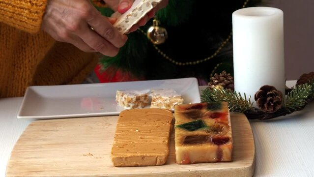 A woman in a yellow knitted sweater breaks a hard almond turron into pieces with her hands.