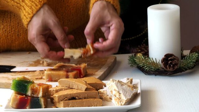 A woman transfers pieces of fruit nougat from a cutting wooden board to a plate.