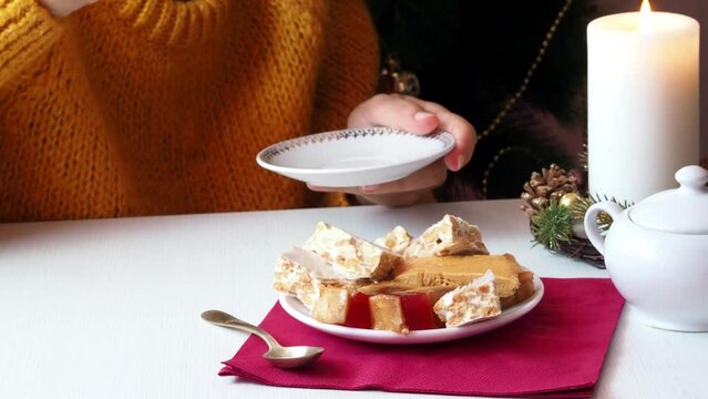 A woman drinks tea from a white porcelain cup and saucer and eats a piece of hard almond turron.