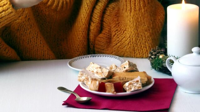 A woman drinks tea from a white porcelain cup, in front of her is a plate with a traditional Spanish dessert - Almond Turron.
