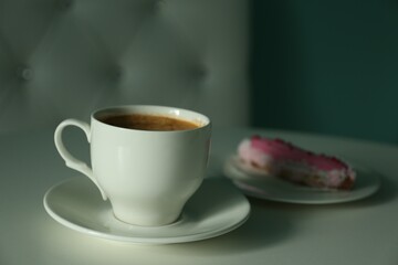 Cup of delicious aromatic coffee and eclair on white table indoors, closeup