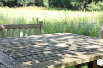 Empty wooden table with bench on sunny day in garden