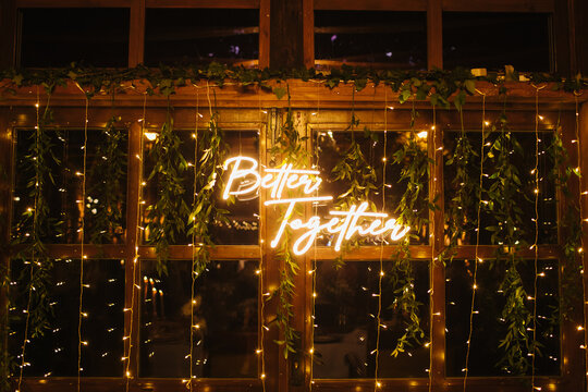 Wedding day neon text. Wedding venue decoration. Boho style leaves decorations. Rustic wedding party in wooden barn with glass windows. Closeup better together banner.