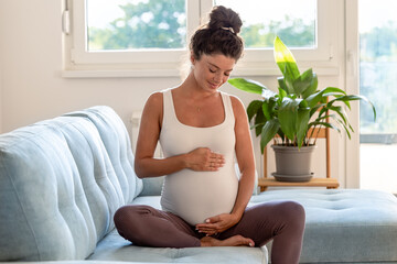 Pregnant woman holding belly on couch at home