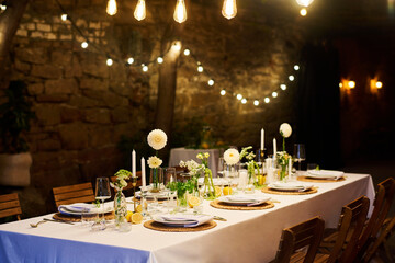 Served festive table with plates, wineglasses, decorations and napkins standing by stone wall in restaurant with illuminations