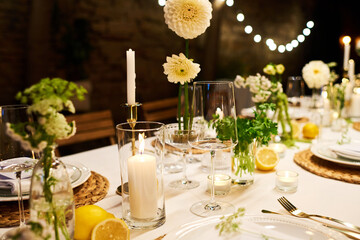 Close-up of dinner table with wineglasses, candles, dahlia flowers and other decorations prepared for wedding feast in luxurious restaurant