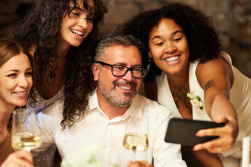 Four happy intercultural well-dressed people gathered for wedding party taking selfie or communicating with friends in video chat