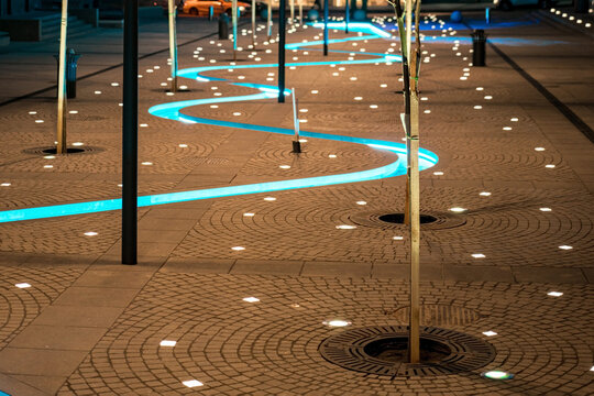 Many ground lamps are installed on the ground and illuminates at night, with artificial blue water flow in the middle. Outdoor. Street. Travel. Eco. Saving. Walk. Energy. Walkway. Bright. Equipment