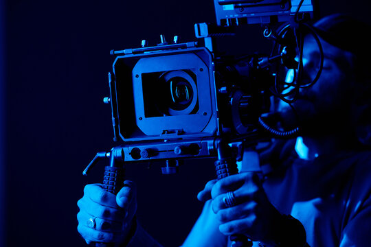 Hands of young videographer or photographer holding by handles on tripod on steadicam while shooting commercial in darkness