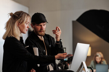 Young female assistant of videographer pointing at computer screen during discussion of new...