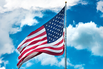 American flag against a cloudy sky. Low angle view of stars and stripes on american flag against blue sky