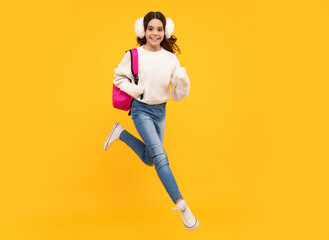 Fototapeta na wymiar Back to school. Teenager schoolgirl with warm hat and sweater on yellow isolated studio background. Jump and run, jumping kids. Winter school.
