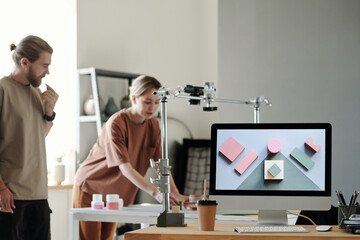 Computer monitor with photo of objects standing on workplace of photographer against his assistant preparing for shooting