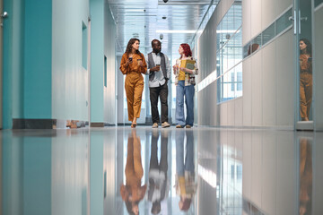 Part of interior of office center and three colleagues walking along corridor and having discussion...