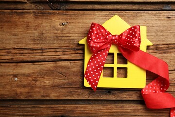 Yellow house model with bow on wooden table, top view and space for text. Housewarming party