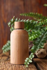 Wooden bottle of cosmetic product and green leaves on table