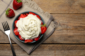 Bowl with delicious strawberries and whipped cream served on wooden table, flat lay. Space for text