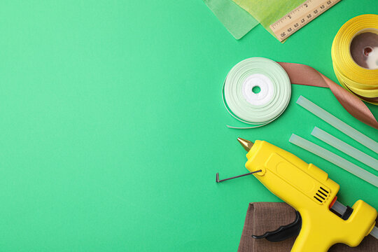 Hot glue gun and handicraft materials on green background, flat lay. Space for text