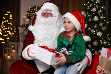 Fototapeta na wymiar Santa Claus giving present to little girl in room decorated for Christmas