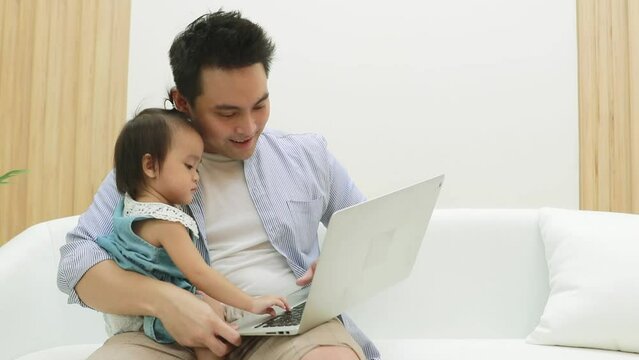 Super dad single dad sitting on the sofa playing laptop with daughter and raising the mischievous daughter in the cute and happy home.