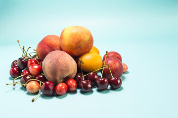 A large mountain of fresh fruit bananas, cherries, nectarines, apricots, peaches on a bright blue background is a place for text.
