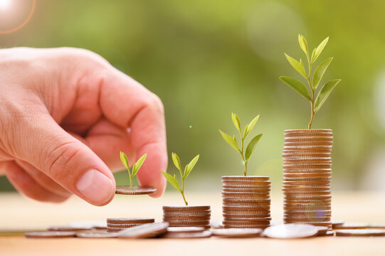 Close up of male hand stacking coins with green bokeh background, Business Finance and Money concept, Save money for prepare in the future. Trees growing on coin..