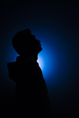 Cleanly define silhouette of man looking up wearing hood blue background