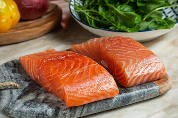 two pieces of raw salmon, on the stone board with bell peppers and fresh arugula in the background