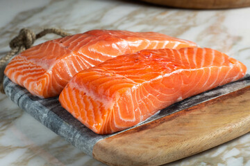 two pieces of raw salmon, on wooden board and marble table