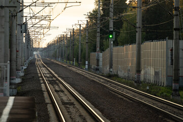 Fototapeta na wymiar Empty railway tracks with green light semaphore at sunset, forest on background. Perspective of electrified high-speed railroad. Transportation concept. 