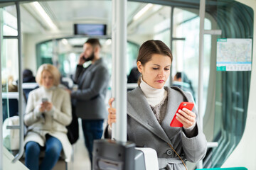 Fototapeta na wymiar Positive woman reading from mobile phone screen in tram