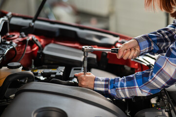 Obraz na płótnie Canvas Female auto mechanic unscrewing a nut to replace a car spark plug.