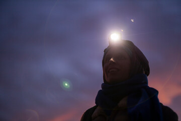 Dreamy Portrait of Female Hiker with headlight at Dusk Looking up in the Sky of Darkness and Stars