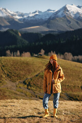 Fototapeta na wymiar Woman fall stands a smile travels to the mountains in nature on a hike and happiness in a yellow raincoat against the snowy mountains in the sunset, freedom of life style