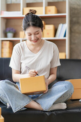 Asian woman working at home with yellow box and laptop for taking orders, sme business ideas on parcel delivery
