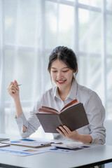 Asian woman working at home on desk using calculator to calculate tax accounting expense report with graph document and laptop computer.