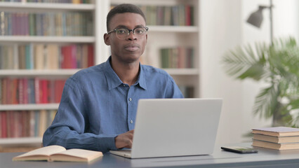 Young African Man Looking at Camera while using Laptop