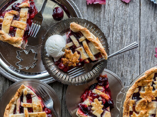Slices of cherry pie on shiny metal plates on a rustic wooden board.