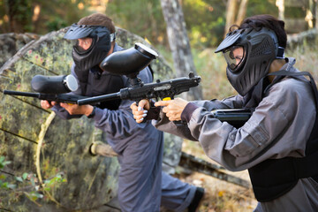Fototapeta premium Woman targeting with paintball gun to eliminate enemies on battlefield. Team shooting with paintball markers.