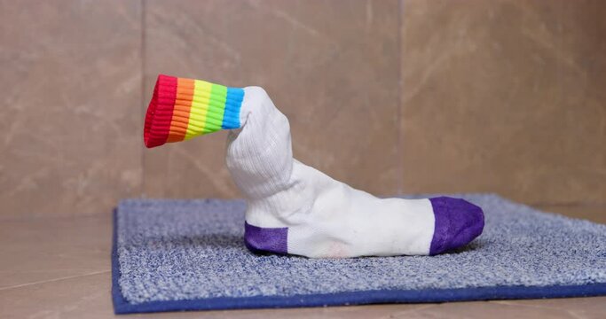 One sock stands on floor in bathroom on rug. Dirty stinky sock joke. Fashionable socks with bright pattern. Stylish minimalist clothing with bright color accents. Socks scattered around apartment