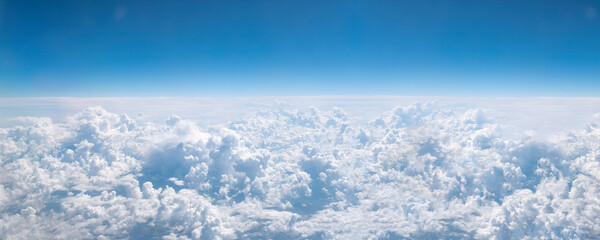 Over clouds. Banner with blue sky and white cumulus cloud. Aerial view from airplane window.