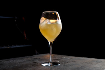 refreshing yellow cocktail served in a glass with ice inside a bar with a black background