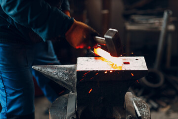 Blacksmith forges and makes metal detail with hammer and anvil at forge. Motion blur