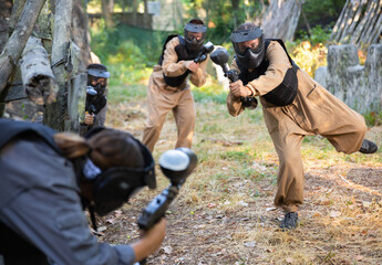 Fototapeta premium Team eliminating opponents on paintball field. People in protective outwear and helmets aiming with paintball markers.