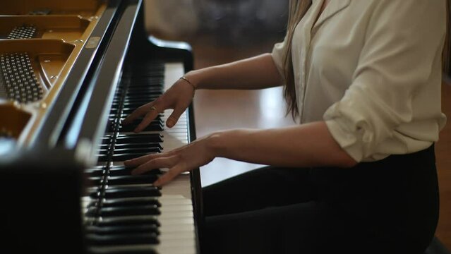 Close-up cropped shot of unrecognizable elegance pianist female playing gentle classical music on beautiful grand piano with open lid. Closeup of hands gracefully pressing keys of musical instrument.