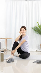 Fototapeta na wymiar Beautiful Asian woman in sportswear is warming up or doing light exercises in the house with dumbbells and a protein shake or bottle of water and using a laptop at home, Healthy exercise.